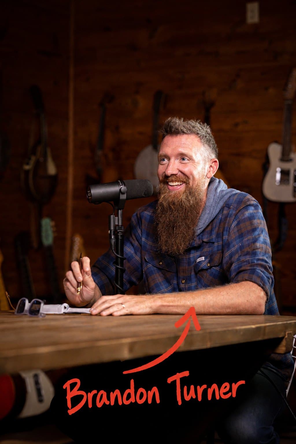 Brandon Turner smiling behind a podcast microphone in his studio